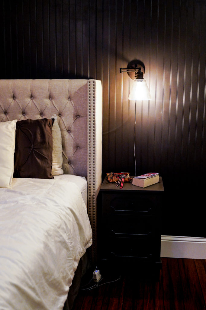 Industrial plug-in wall sconces in dark paneled bedroom