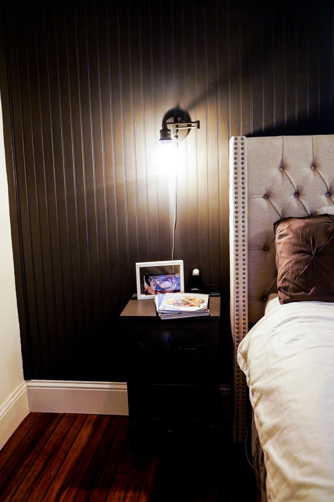 Industrial plug-in wall sconces in dark paneled bedroom